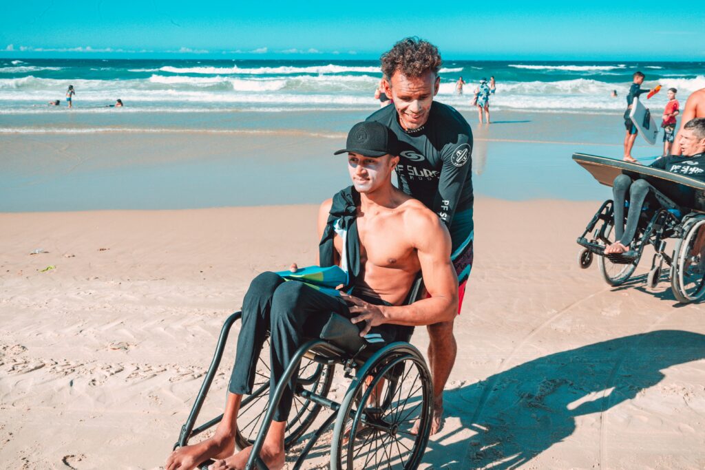 guy being pushes in wheelchair through sand