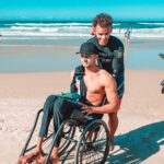 guy being pushes in wheelchair through sand